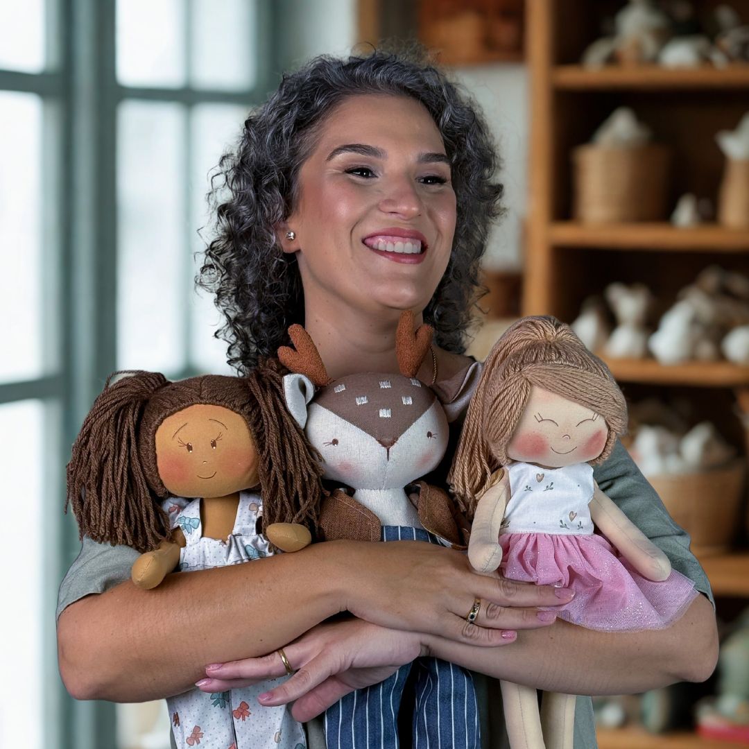 Mônica sorrindo segurando três bonecas de pano feitas à mão